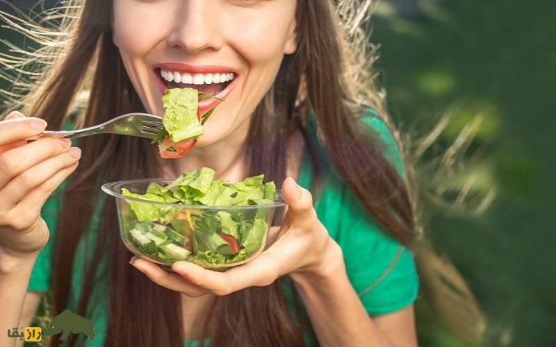زنی در حال خوردن سالا در یک ظرف شیشه ای
